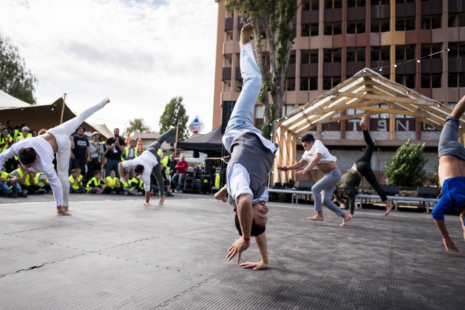 Performance du groupe acrobatique de Tanger lors du KM4 à La Courneuve, acrobates réalisant des figures avec en arrière-plan le public en gilets jaunes de chantier, de jour 