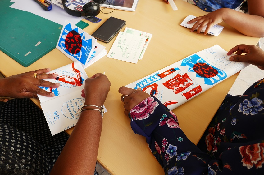 Deux enfants tiennent des livrets entre leurs mains à une table dans le cadre du projet « Ligne Z », chantier partagé du collectif « Ne Rougissez Pas » autour de la gare de Vitry-Centre