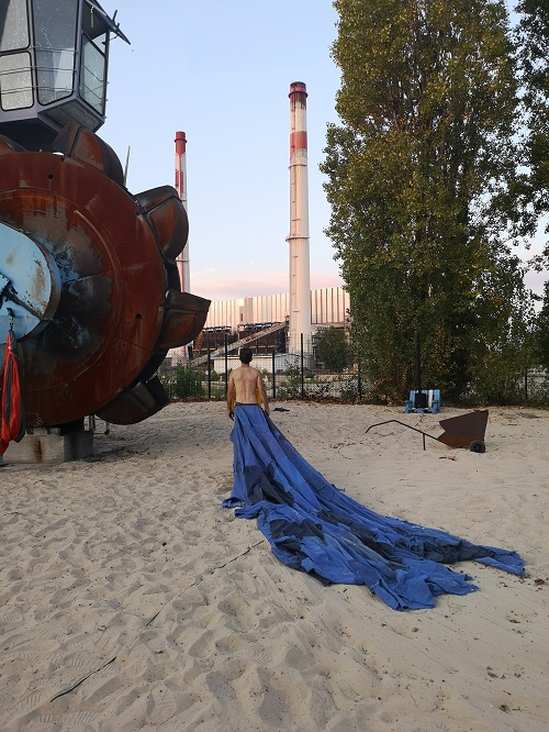 Un engin de chantier avec une roue de grande taille et un danseur avec un grand tissu, dans le cadre du projet de la Compagnie Tangible à Vitry-sur-Seine